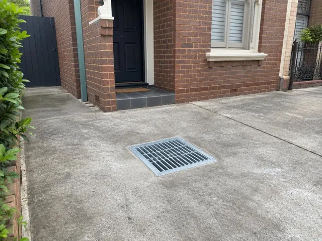 Concrete driveway with a clean metal drain grate beside a brick house in Annandale