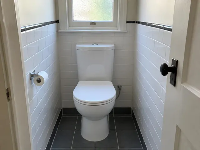 Clean white toilet in a small tiled bathroom with window and dark floor tiles in Stanmore
