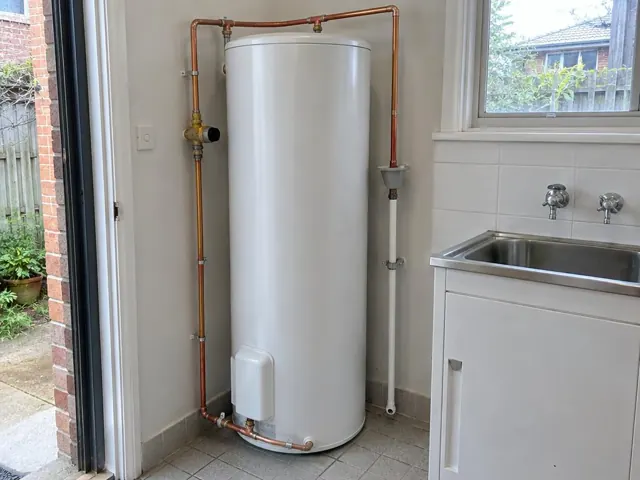 White hot water cylinder beside a laundry sink and tiled wall in a home interior in Annandale