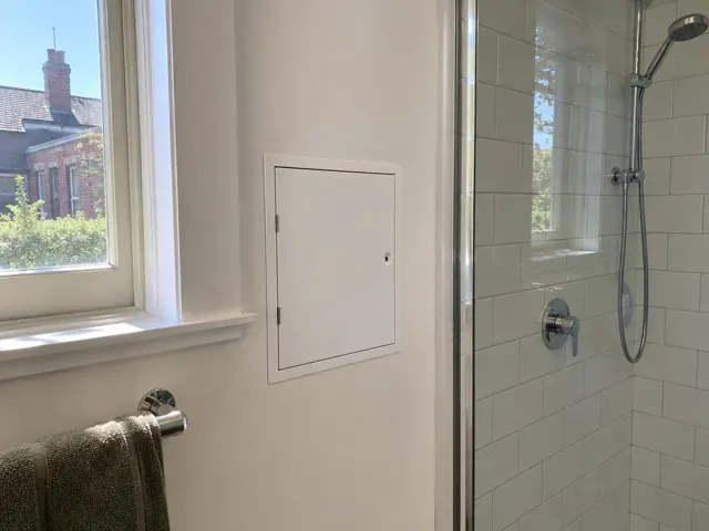 Neat white access panel on a painted bathroom wall beside a shower and window in Lilyfield